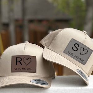 May include: Two beige trucker hats with brown patches. The patches have a letter, a heart, and the date "VI.XV.MMXXIV". One hat has the letter "R" and the other has the letter "S".