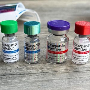 Four bottles of medication labeled "Tirzepatide Injection" are arranged on a wooden surface.