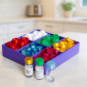 May include: A purple divided tray filled with colorful bottle caps in red, white, green, blue, yellow, and pink. Three small glass vials with yellow, green, and blue caps are in front of the tray. One vial has a graphic of an atom.