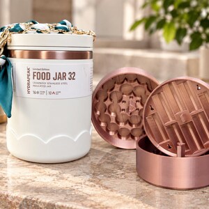 May include: A white Hydrapeak Food Jar 32 with a rose gold band and lid. The label reads Limited Edition Food Jar 32 Leakproof Stainless Steel Insulated Jar 16 Hours Cold 10 Hours Hot. A teal and white patterned scarf is tied to the top handle.