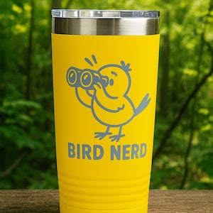 May include: Yellow tumbler with a silver lid featuring a cartoon bird with binoculars and the text "BIRD NERD" in gray. The tumbler is cylindrical with a ridged design near the bottom.