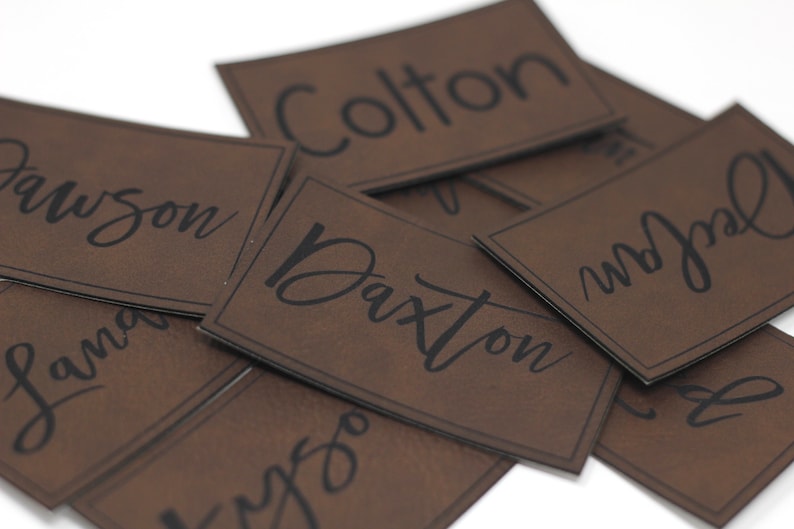 May include: A pile of brown leather name tags with black lettering. The names on the tags are: Dawson, Landon, Colton, Daxton, and  "Mr. Joel".