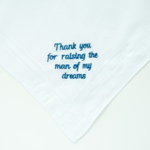 Puede incluir: Pa&ntilde;uelo blanco con texto bordado en azul que dice: "Thank you for raising the man of my dreams". El pa&ntilde;uelo est&aacute; doblado en una esquina y tiene un dise&ntilde;o sencillo y elegante.