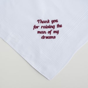 Puede incluir: Pa&ntilde;uelo blanco con un patr&oacute;n texturizado y texto bordado en color burdeos. El texto dice "Thank you for raising the man of my dreams". El pa&ntilde;uelo est&aacute; doblado y se muestra sobre un fondo claro.