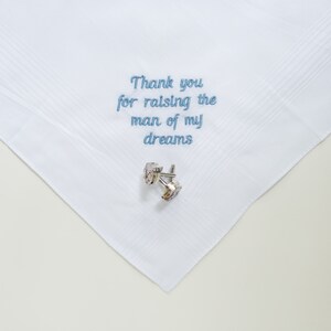 Puede incluir: Pa&ntilde;uelo blanco con texto bordado en azul que dice "Thank you for raising the man of my dreams". Un par de gemelos plateados con piedras transparentes descansa sobre el pa&ntilde;uelo. El pa&ntilde;uelo tiene un sutil estampado a rayas.