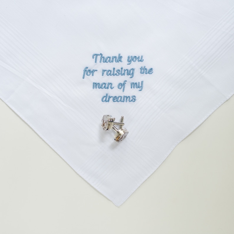 Puede incluir: Pa&ntilde;uelo blanco con texto bordado en azul que dice "Thank you for raising the man of my dreams". Un par de gemelos plateados con piedras transparentes descansa sobre el pa&ntilde;uelo. El pa&ntilde;uelo tiene un sutil estampado a rayas.