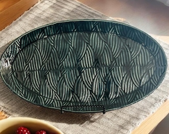 May include: A dark green oval serving platter with a raised leaf pattern. The platter is made of ceramic and has a glossy finish.