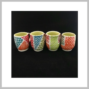 Könnte beinhalten: Vier handgefertigte Keramikbecher mit farbenfrohen, geometrischen Designs. Jeder Becher hat ein einzigartiges Patchwork aus Texturen und Mustern in Rot-, Blau-, Grün- und Orangetönen. Die Innenseiten sind hellgrün und die Griffe sind neutral.