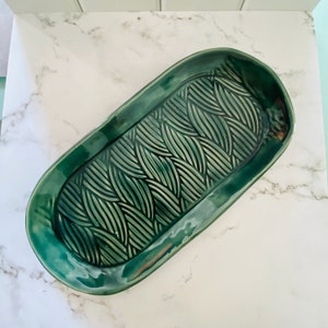May include: A green oval ceramic serving tray with a raised, textured design of overlapping leaves.