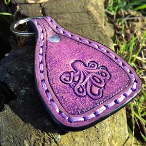 May include: Purple leather keychain with a stitched border and an embossed octopus design.