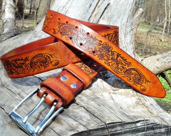 Könnte beinhalten: Ein brauner Ledergürtel mit einer silbernen Schnalle. Der Gürtel ist mit einem komplizierten floralen Muster verziert, das in das Leder gebrannt wurde.