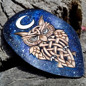 May include: A leather owl pendant with a Celtic knot design, painted with a blue and white galaxy background and a white crescent moon.
