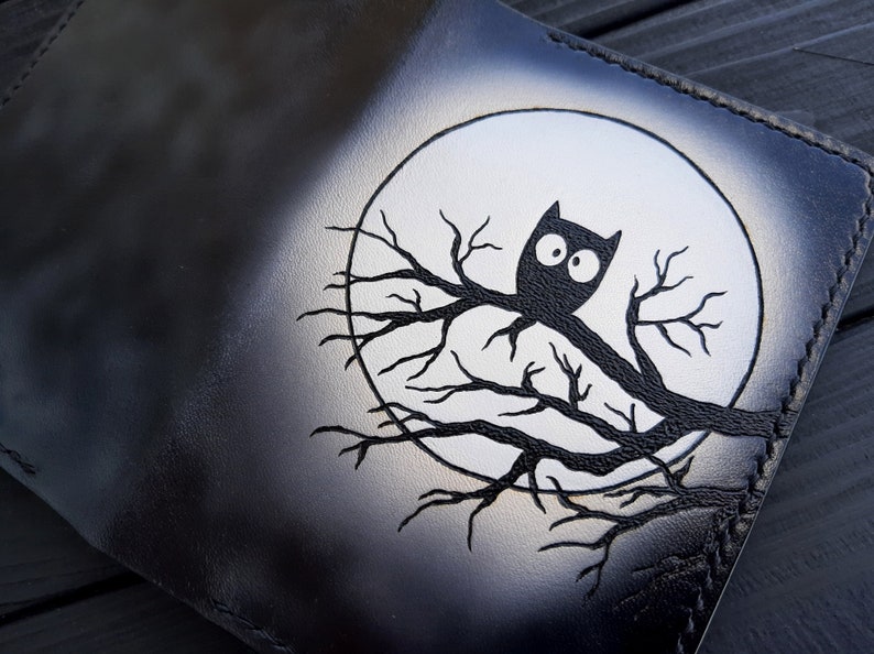 May include: Black leather wallet with a white moon and a black owl perched on a branch. The owl has large, white eyes.