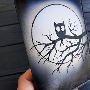 May include: Black leather notebook with a white moon and a black owl perched on a branch. The owl has large, round eyes.
