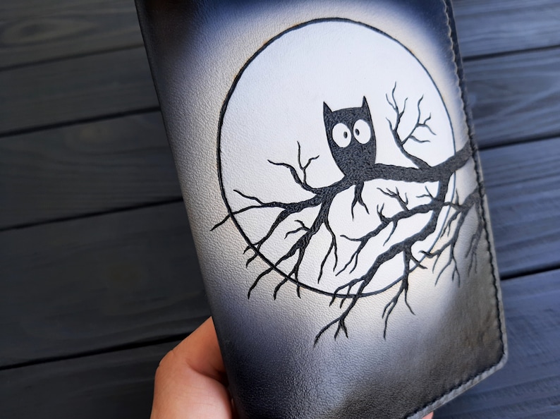 May include: Black leather notebook with a white moon and a black owl perched on a branch. The owl has large, round eyes.