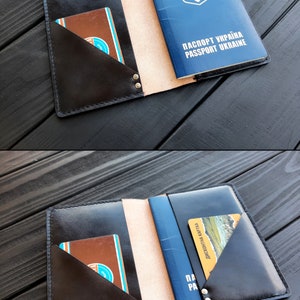 May include: A black leather passport holder with a beige interior and two pockets for cards. The holder is open and a blue passport with the Ukrainian coat of arms and the text "ПАСПОРТ УКРАЇНА PASSPORT UKRAINE" is visible.
