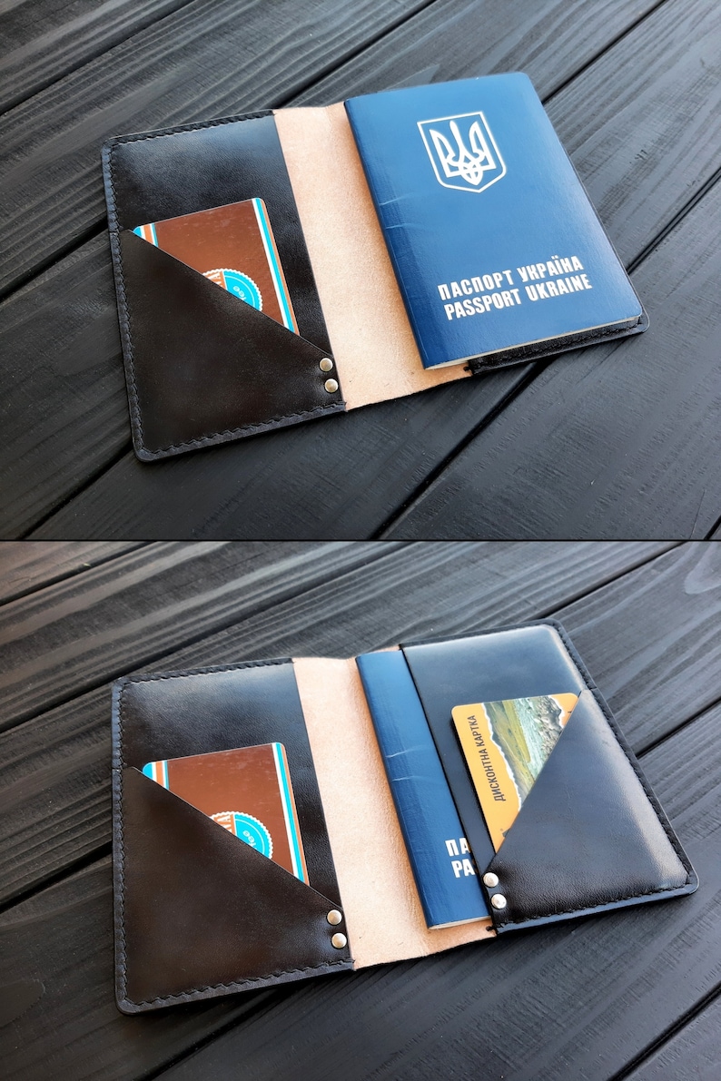 May include: A black leather passport holder with a beige interior and two pockets for cards. The holder is open and a blue passport with the Ukrainian coat of arms and the text "ПАСПОРТ УКРАЇНА PASSPORT UKRAINE" is visible.