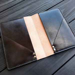 May include: A black leather notebook cover with a brown interior and silver rivets. The cover is folded open to reveal the interior.