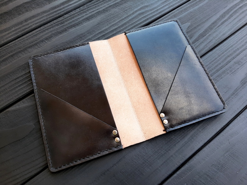 May include: A black leather notebook cover with a brown interior and silver rivets. The cover is folded open to reveal the interior.