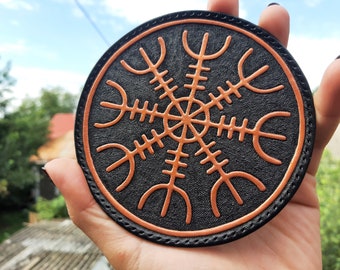 Könnte beinhalten: Ein runder Lederuntersetzer mit schwarzem Hintergrund und einem orangefarbenen Vegvisir-Symbol. Der Untersetzer ist am Rand vernäht.