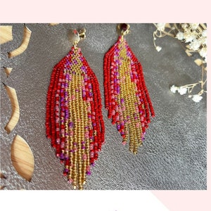 Puede incluir: Un par de aretes largos de flecos de cuentas en rojo, dorado y morado. Los aretes están hechos con punto de ladrillo y tienen un diseño de flecos. Los aretes se muestran sobre un fondo blanco con el texto "FRINGE BEADED EARRINGS PATTERN AND TUTORIAL DIGITAL PDF FILES ARE INSTANT DOWNLOAD BRICK STITCH PATTERN" sobre los aretes.