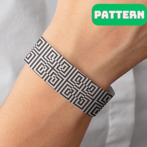 May include: A black and white geometric pattern wristband. The pattern is a repeating design of squares and rectangles.