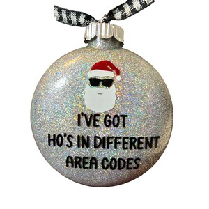 May include: A silver glitter Christmas ornament with a Santa Claus wearing sunglasses and the text "I've got ho's in different area codes".