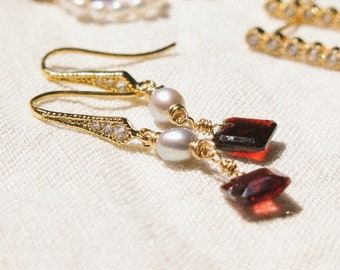 May include: Gold dangle earrings with a red gemstone, a pearl, and small clear rhinestones.