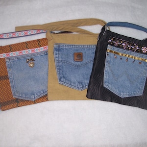 May include: Three different denim bags with fabric straps. The bags are made from recycled denim and have different fabric accents. One bag has a brown and orange patterned fabric, another has a brown fabric, and the third has a black fabric with gold accents.