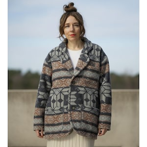 Peut inclure: Veste à motifs dans les tons de gris, marron et crème. La veste présente un motif géométrique et une coupe blazer classique avec deux poches avant. La veste est portée sur un haut blanc et une jupe crème.