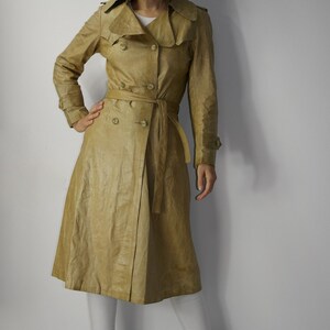 May include: A light brown leather trench coat with a double-breasted closure, a belt, and long sleeves.