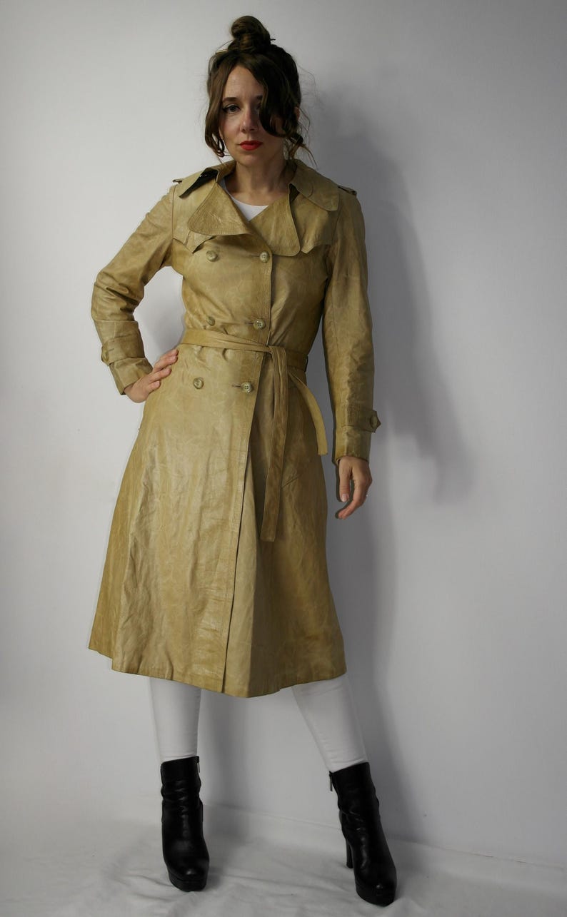 May include: A light brown leather trench coat with a double-breasted closure, a belt, and long sleeves.
