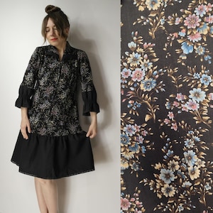 May include: A black dress with a floral pattern and long sleeves. The dress features a ruffled hem and cuffs. The floral pattern includes pink, blue, and yellow flowers on a black background. The dress is knee-length.