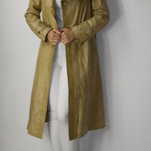 May include: A long, tan leather trench coat with a double breasted closure and a belt. The coat has a classic design and is made of a high-quality leather.