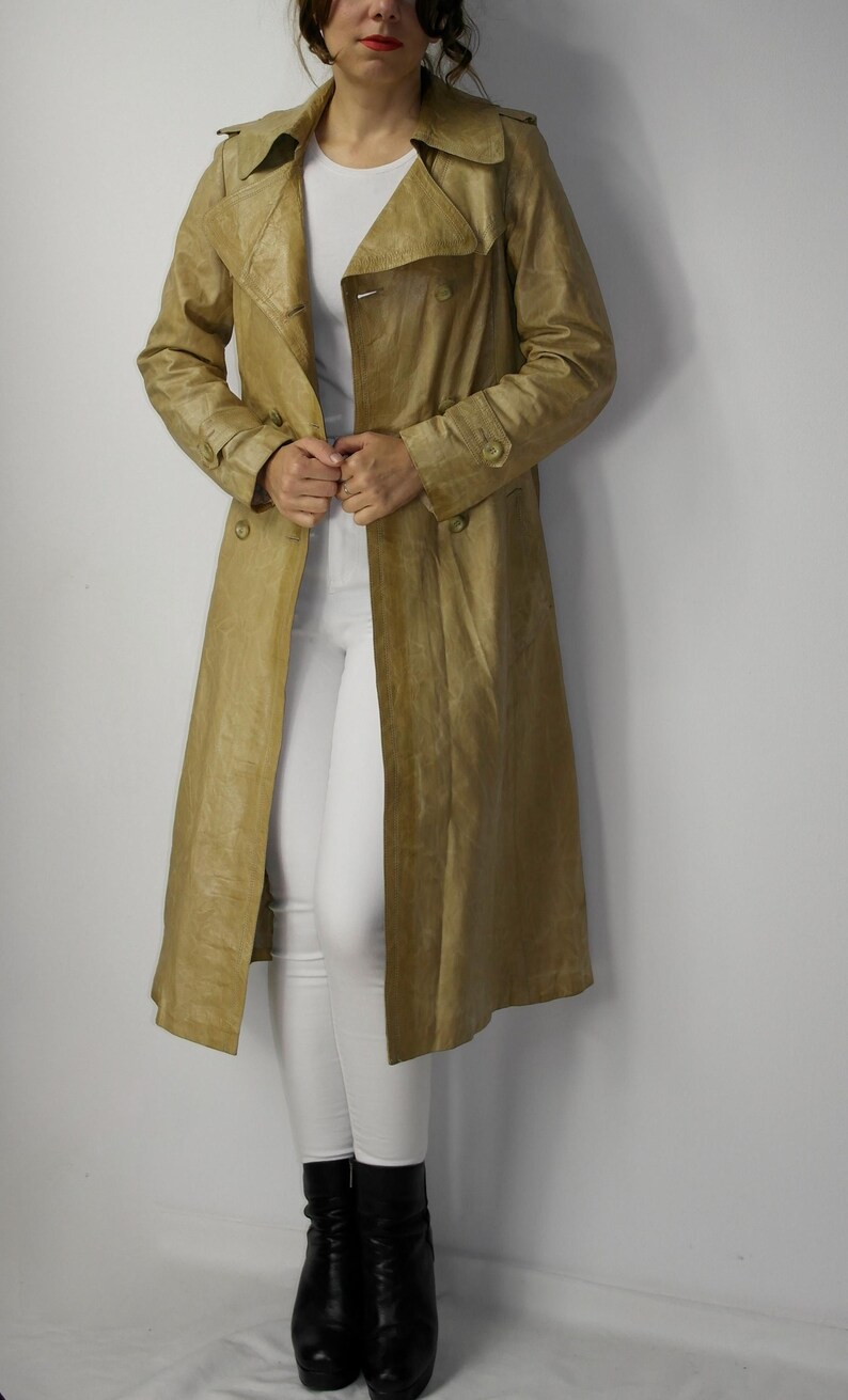 May include: A long, tan leather trench coat with a double breasted closure and a belt. The coat has a classic design and is made of a high-quality leather.