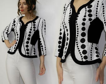 May include: A black and white patterned jacket with a zip closure. The jacket has a fitted silhouette and a curved hemline. The pattern features large black polka dots on a white background.