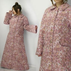 Puede incluir: Un abrigo largo con botones con un estampado floral en tonos rosa, blanco y amarillo. El abrigo tiene cuello redondo, bolsillos y mangas largas. La tela parece acolchada. El abrigo es hasta la rodilla y tiene una falda acampanada.