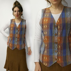 Puede incluir: Un chaleco estampado con cuello en V y botones de madera. El chaleco presenta una mezcla de diseños geométricos naranjas, azules y marrones. Se usa sobre una camisa blanca de manga larga y se combina con una falda marrón.