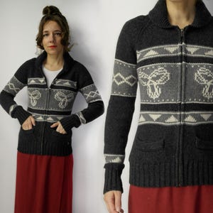 Può includere: Un cardigan di maglia grigia con chiusura a zip e un motivo geometrico bianco e grigio. Il cardigan ha due tasche e un colletto.
