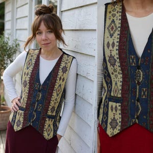 May include: A sleeveless vest featuring a multi-colored woven pattern in shades of cream, deep red, and navy blue. The garment has a V-neckline, a front button closure with four dark buttons, and two small front pockets with matching patterned flaps.