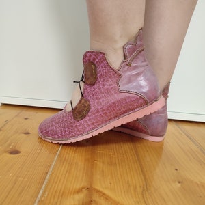 May include: Pink leather ankle boots with a lace-up closure and a pink sole. The boots have a distressed look and a unique design.
