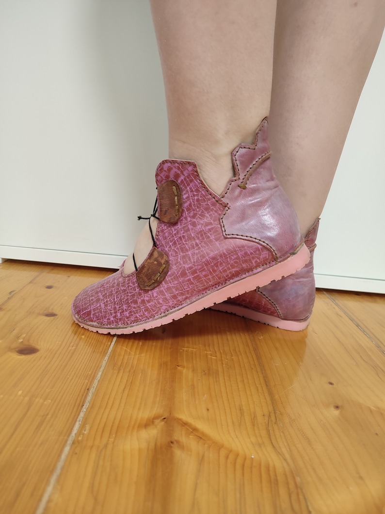 May include: Pink leather ankle boots with a lace-up closure and a pink sole. The boots have a distressed look and a unique design.