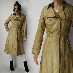 May include: A long, beige leather trench coat with a double-breasted closure, a belt, and a collar. The coat has a classic design and is made of a high-quality leather.