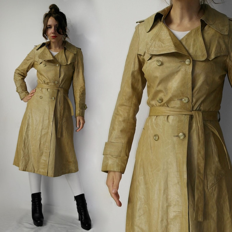 May include: A long, beige leather trench coat with a double-breasted closure, a belt, and a collar. The coat has a classic design and is made of a high-quality leather.