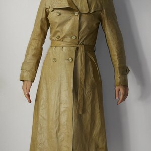 May include: A long, tan leather trench coat with a double-breasted closure, a belt, and a collar.