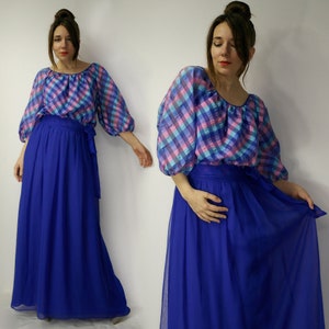 May include: A vintage two-piece outfit featuring a long, flowing royal blue skirt and a plaid top. The top has a scoop neckline and puffy sleeves with a pattern of pink, blue, and teal squares. The skirt has a matching blue sash.