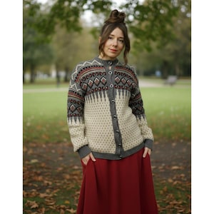 Può includere: Un cardigan fantasia grigio, crema e rosso, con chiusura a bottoni e collo alto. La persona indossa una lunga gonna rossa. Lo sfondo è un parco con erba verde e alberi. Il cardigan ha maniche lunghe.