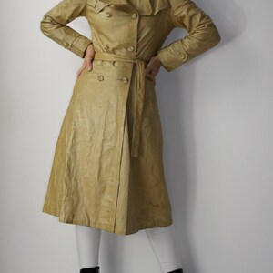 May include: A long, light brown leather trench coat with a double breasted closure, a belt, and a wide collar.