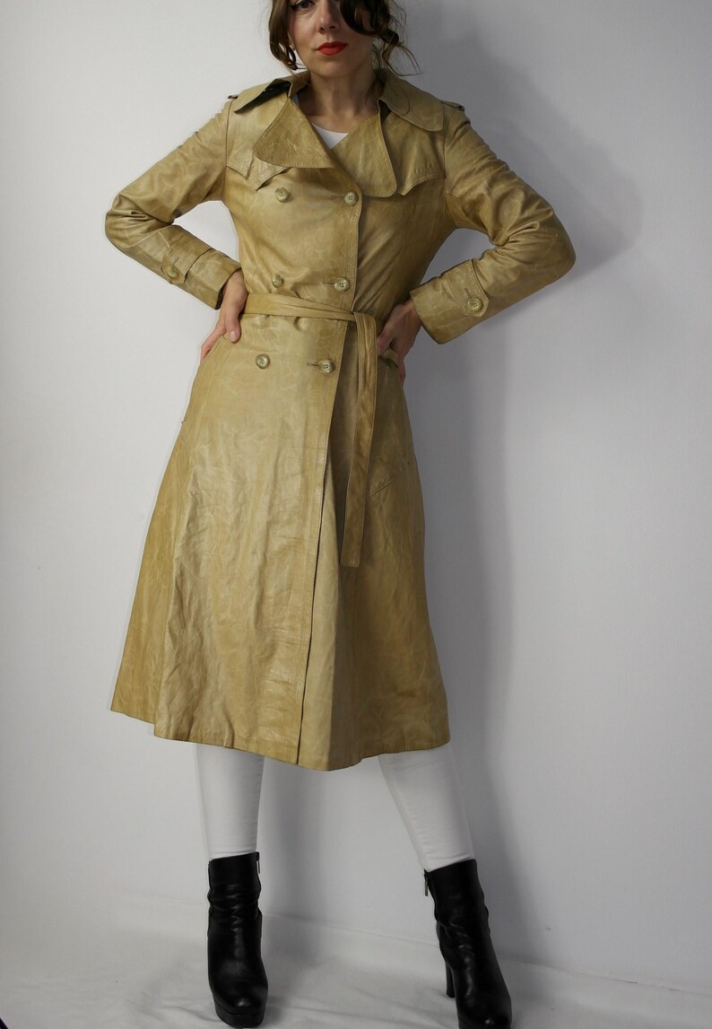 May include: A long, light brown leather trench coat with a double breasted closure, a belt, and a wide collar.