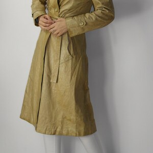 May include: A long, tan leather trench coat with a double-breasted closure, a belt, and a collar that can be worn up or down.